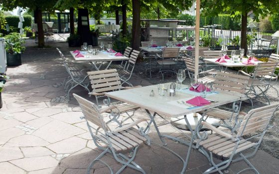 Neben einem kleinen Gehweg stehen mehrere, gedeckte Gartentische und Stühle. 