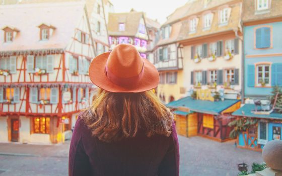 Frau mit orangefarbenem Hut blickt auf historische Fachwerkhäuser in der Altstadt von Strassburg im Elsass.