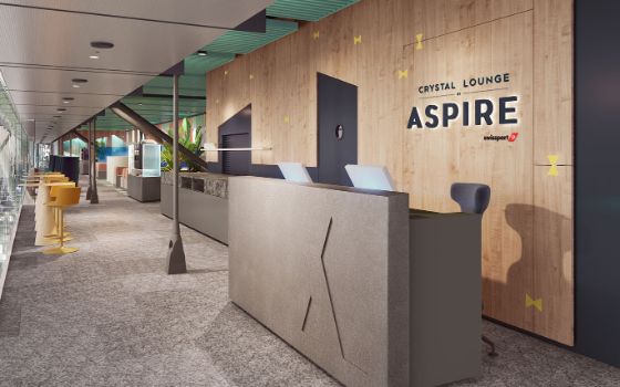 Eingangsbereich mit Empfangstheke vor einer Holzwand mit dem Schriftzug Crystal Lounge by Aspire und dem Swissport Logo in einer hellen Lounge mit modernen Einrichtungselementen.