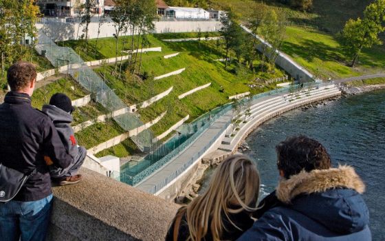 Blick auf den BärenPark in Bern mit terrassierten Grünflächen und Gehegen am Ufer der Aare, beobachtet von Besucherinnen und Besuchern.