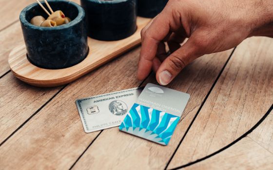 Nahaufnahme einer männlichen Hand an einer Oriental Mandarin Zurich Hotelkarte auf einer silbernen Kreditkarte von American Express auf einem Holztisch, daneben kleine Schalen mit Oliven.