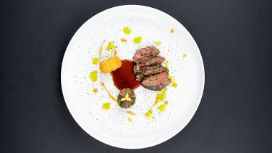 Auf einem weissen Teller liegen vier kleine Stücke von gebratenem Fleisch mit einem Klecks brauner Sosse und einer Krokette.