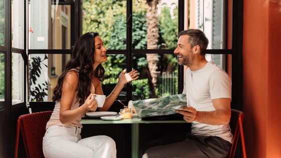 Paar geniesst entspannten Café-Besuch, sitzt an einem Tisch bei Kaffee und Croissants, American Express Vorteile erleben.