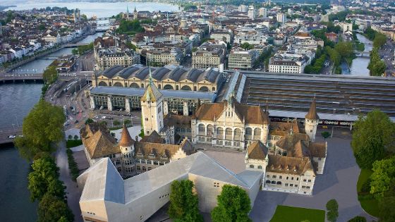 Das Landesmuseum Zürich aus der Luft, das alte Gebäude besteht aus Türmen und verzierten Fenstern und ist direkt mit dem modernen Neubau verbunden, der eine zackige und längliche Form hat.