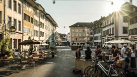 Menschen sitzen in der Abendsonne auf einem Platz in der Altstadt von Winterthur, umgeben von historischen Häusern und Strassencafés.