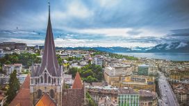Historische Gebäude in Lausanne mit Kathedrale und Alpenpanorama im Hintergrund bei Abendlicht.