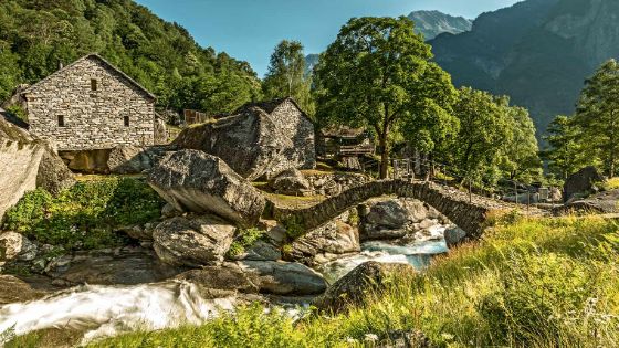 Ein Steinhaus steht vor einem Fluss, über den einen gebogene steinerne Brücke führt.