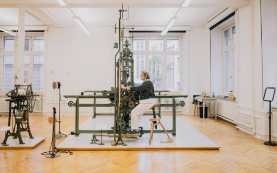 Frau arbeitet an einer historischen Stickmaschine im Textilmuseum St. Gallen, umgeben von lichtdurchfluteten Räumen.